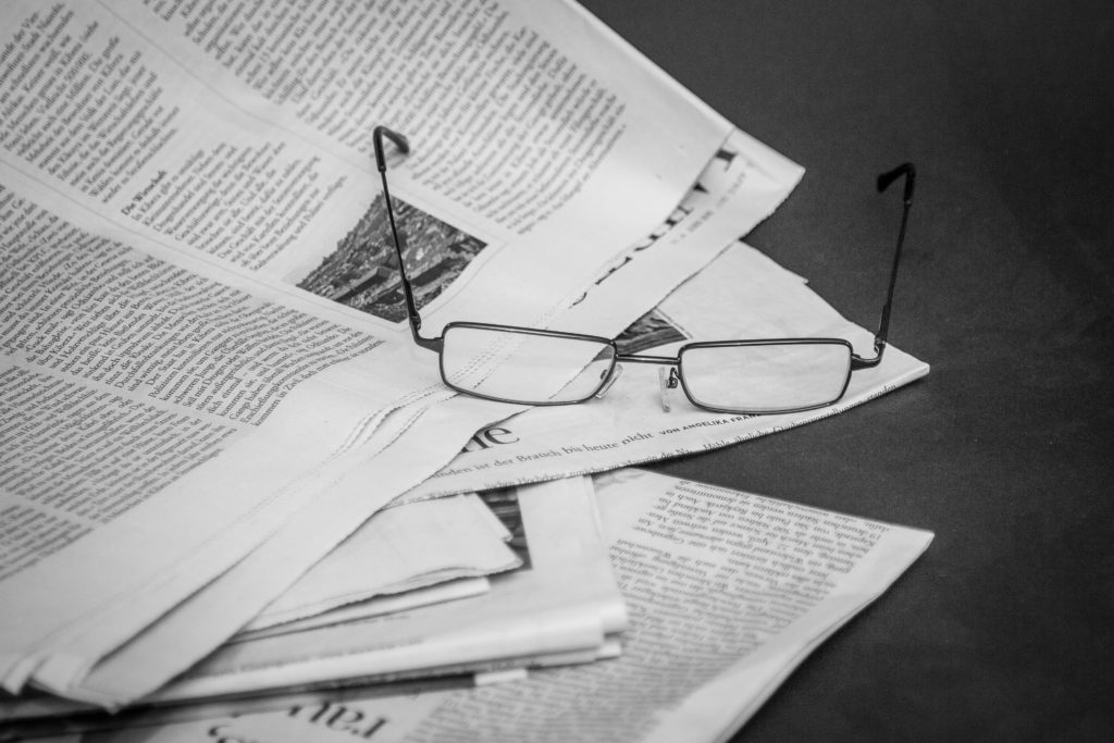 Black and white photo of glasses on spread out newspapers