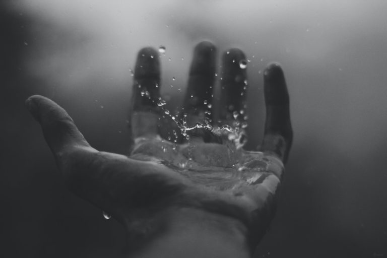 Water droplets falling into open hand. Black-and-white photo.